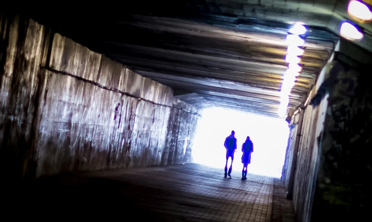 Two figures walking toward bright light in an underpass